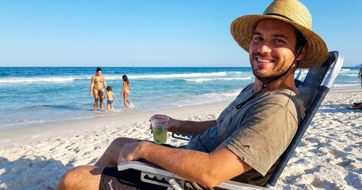 Trabalhador brasileiro feliz na praia em férias remuneradas com família, sol e areia ao fundo