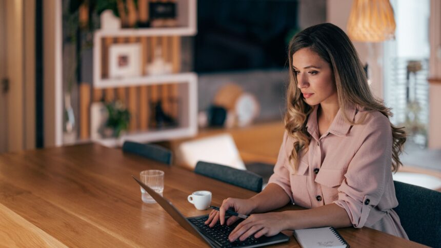 Mulher jovem trabalhando em um laptop em casa, representando o empreendedorismo e a flexibilidade de trabalhar remotamente.