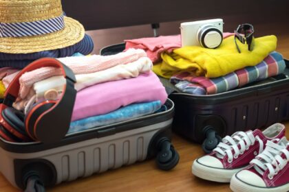 Mala aberta com roupas coloridas, sapatos, chapéu de palha e acessórios de viagem, pronta para férias econômicas.