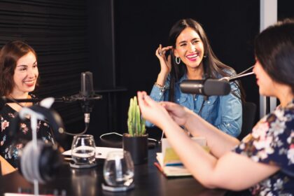 Três mulheres sorrindo enquanto gravam um podcast em um estúdio, representando a troca de ideias e a produção de conteúdo inspirador e informativo.