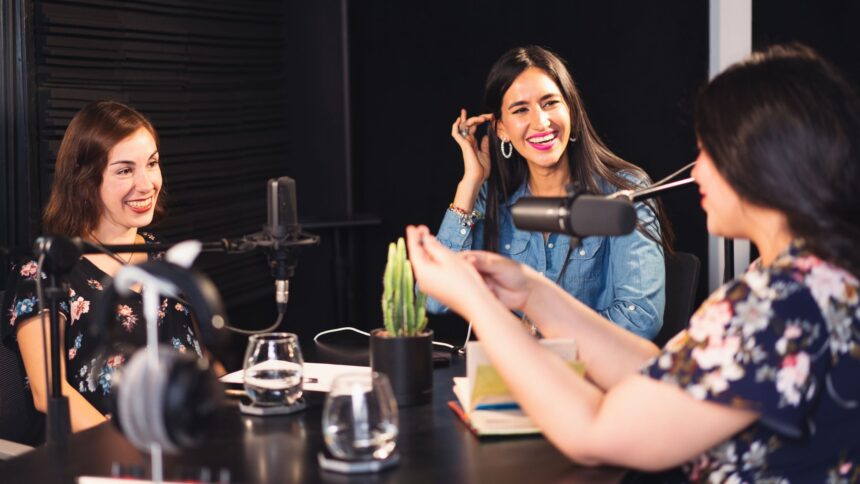 Três mulheres sorrindo enquanto gravam um podcast em um estúdio, representando a troca de ideias e a produção de conteúdo inspirador e informativo.